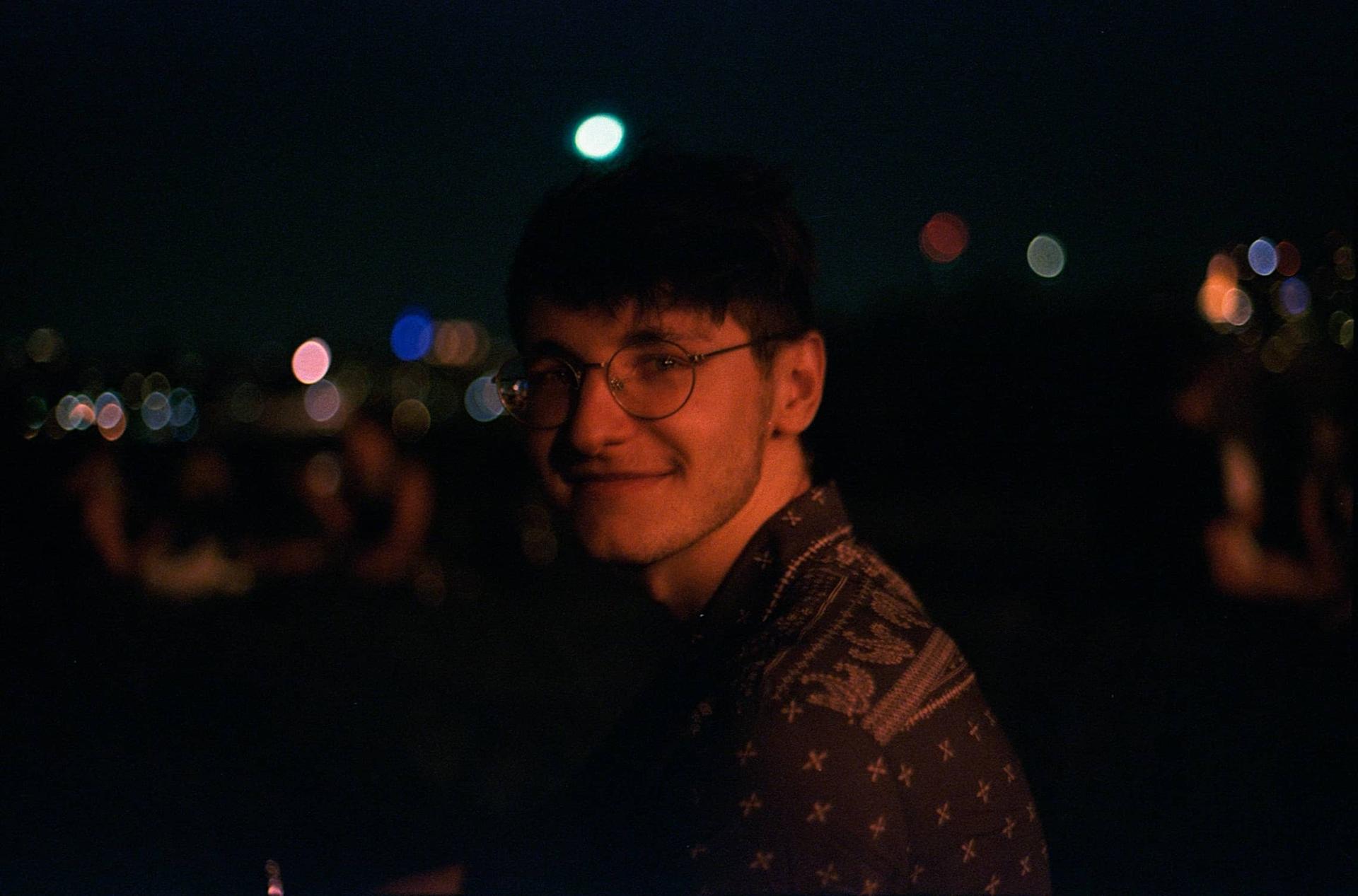 Nathan Sorkin, smiling with a red hue over the photo. With a blurry image of New York city in the background